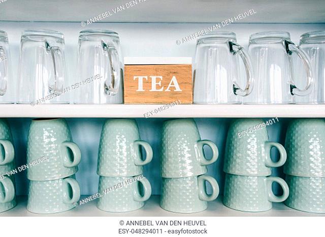 tea cups and coffee mugs on a kitchen shelf with a tea box Rack focus. Close up. wooden shelf