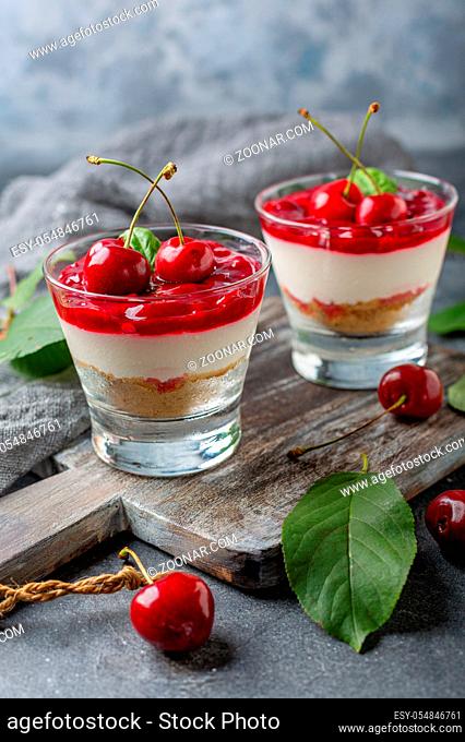 Cheesecake with cherry jelly in glasses and fresh cherry on a wooden serving board. Textured dark background. Selective focus