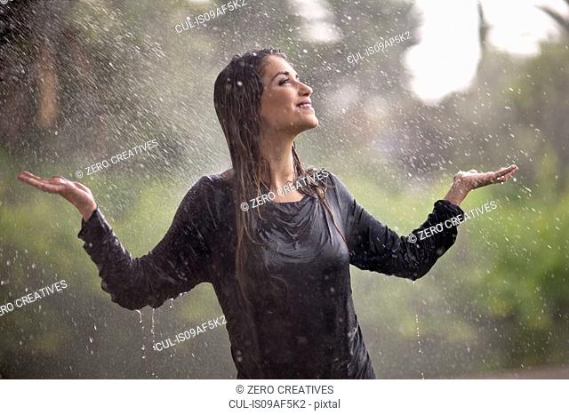 Drenched young woman with arms open in rainy park