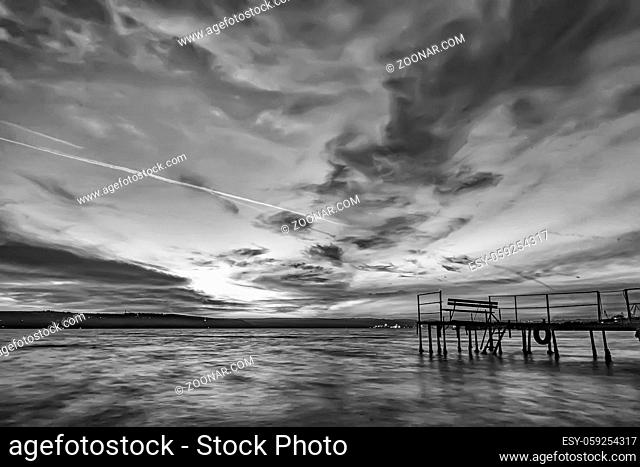 Beautiful black and white long exposure sunset view with bench on wooden pier