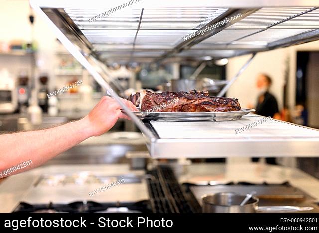 Commercial kitchen background.Chef hand with plate of grilled meat ready to serve . High quality photo