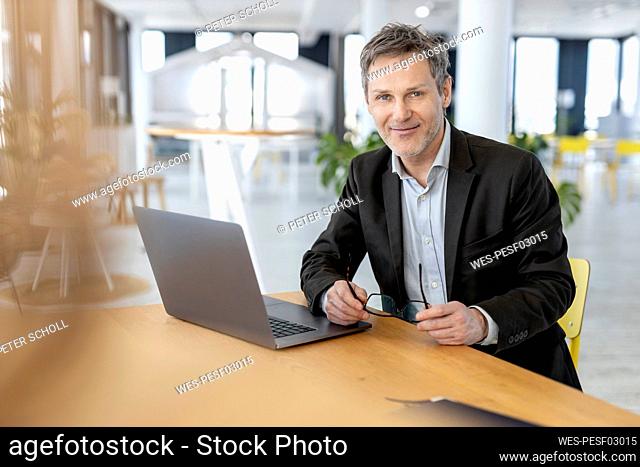 Smiling businessman with laptop sitting at office