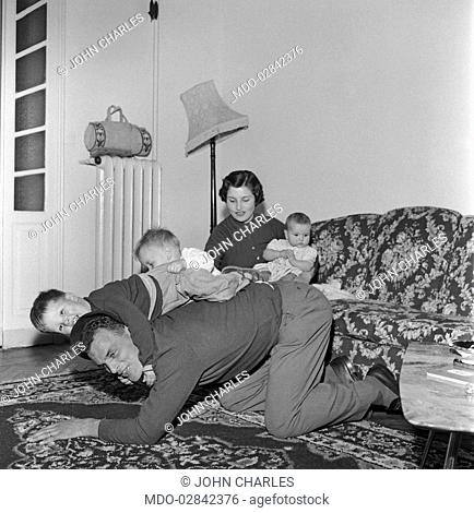 Welsh football player forward of Juventus Football Club John Charles playing with his children beside his wife. Turin, 1957