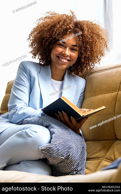 Smiling female professional with book on sofa at home
