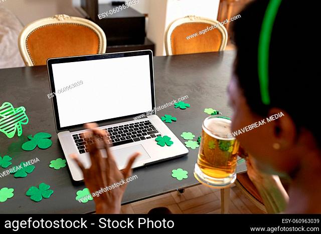 African american woman with beer mug waving at laptop with copy space on video call