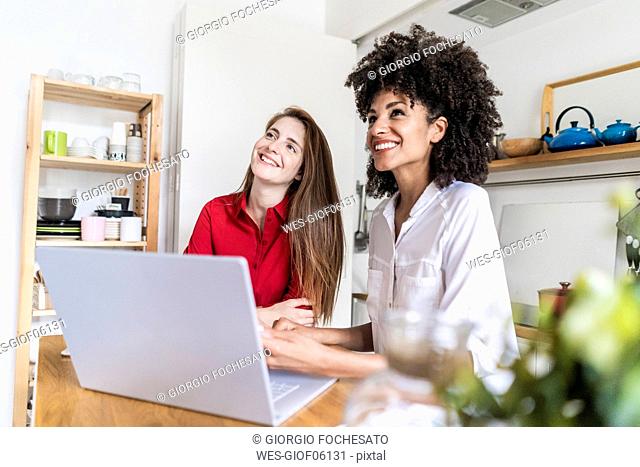 Two women working together in kitchen, using laptop
