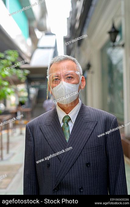 Portrait of mature Japanese businessman with mask and face shield for protection from corona virus outbreak in the city streets