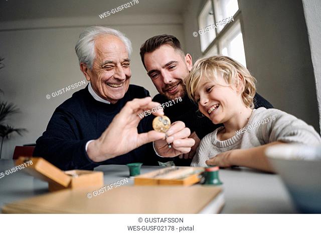 Happy watchmaker showing clockwork to young man and boy