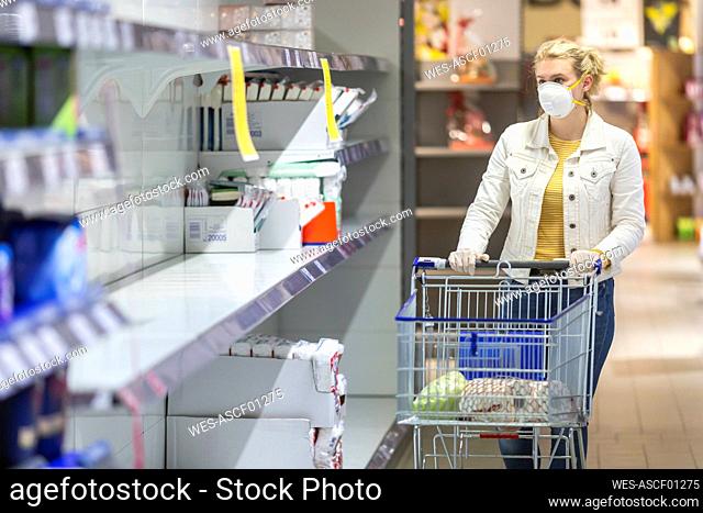 Teenage girl wearing protectice mask and gloves looking at empty shelves at supermarket