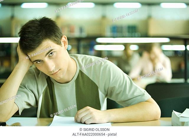 Male student studying in library, looking at camera