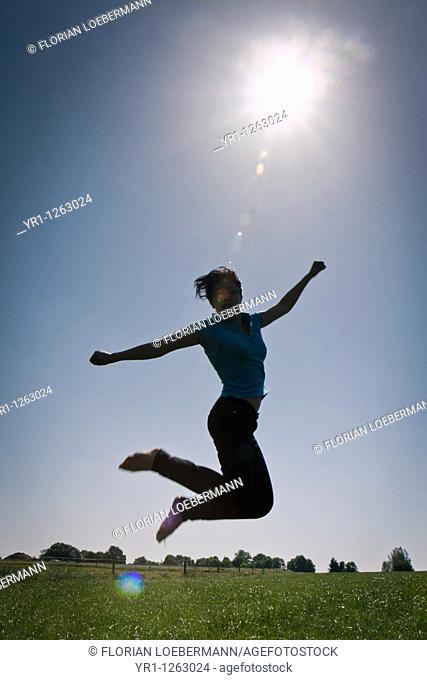 Asian girl jumping in a field during summer. Shot in Aachen, Germany