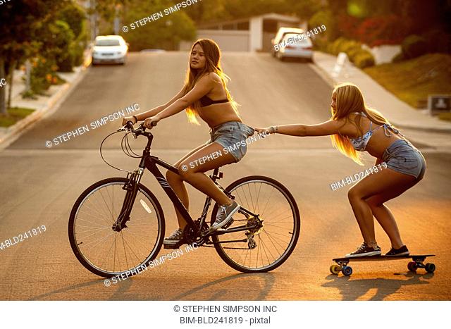 Girl riding bicycle pulling friend on skateboard