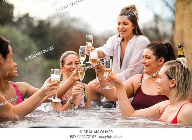 Small group of female friends socialising and relaxing in the hot tub on a weekend away. They are celebrating with a glass of champagne