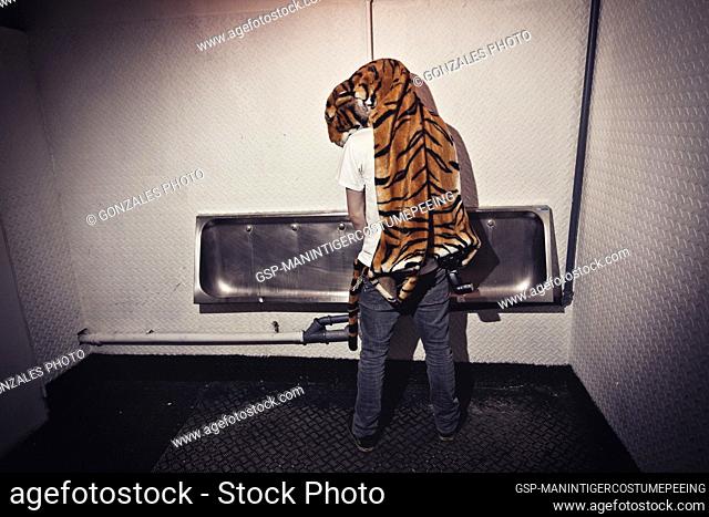A man with a tiger custome on hos shoulders is peeing at a night club toilet. Denmark 2010
