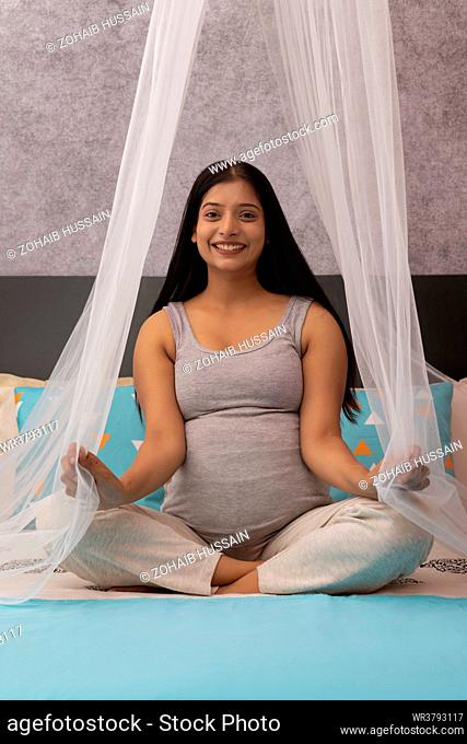Smiling pregnant woman sitting on bed at home