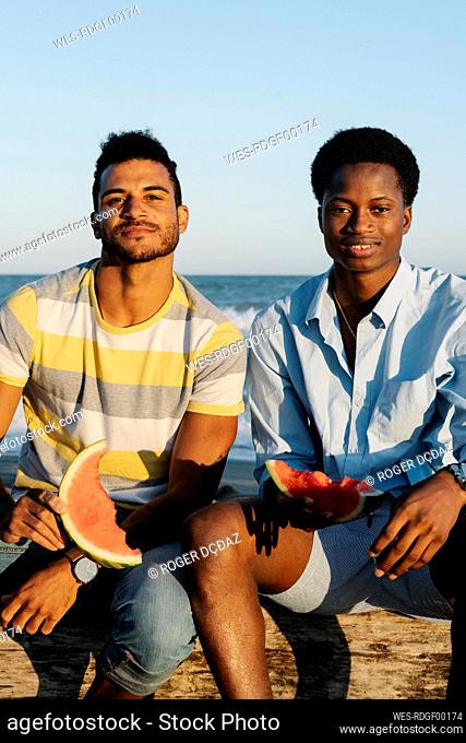 Friends eating watermelon while sitting on beach