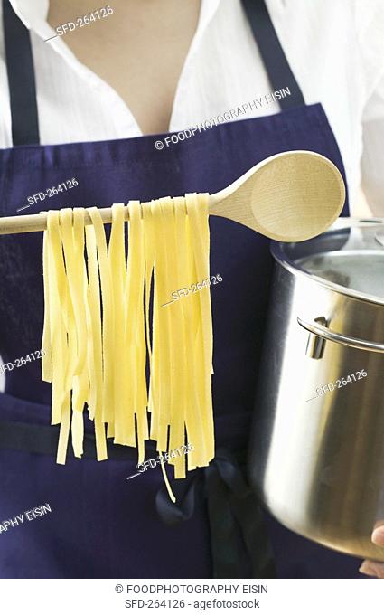 Woman holding pan and home-made pasta on wooden spoon