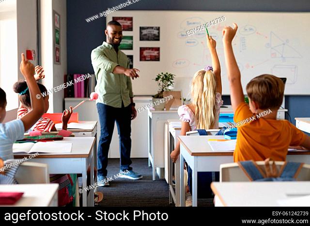 African american young male teacher gesturing on multiracial elementary students with hand raised