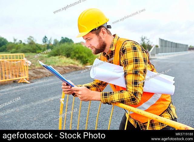 Straßenbauer mit Bauzeichnung schaut auf Checkliste auf der Baustelle vom Straßenbau