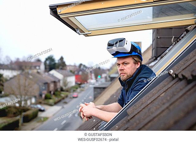 Architect with VR goggles on his safety helmet, looking out of rooflight