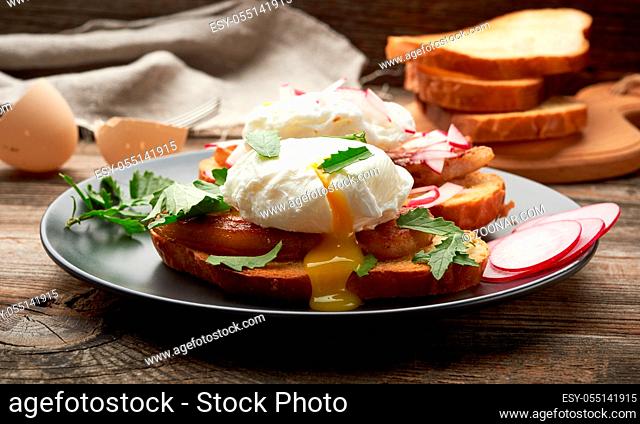 sandwiches on a toasted white slice of bread with poached eggs, green leaves of arugula and radish in a round plate, morning breakfast