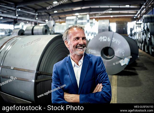 Happy businessman standing with arms crossed in steel mill