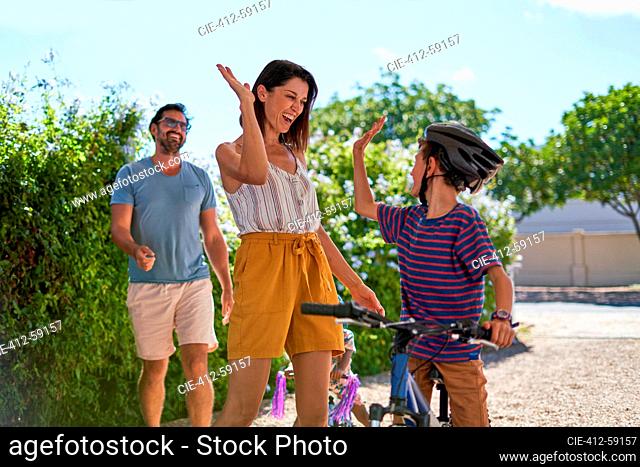 Happy mother and son high fiving in sunny driveway