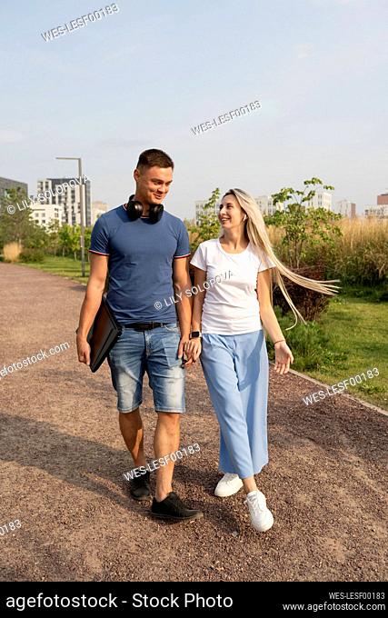 Happy boyfriend and girlfriend walking together holding hands in park