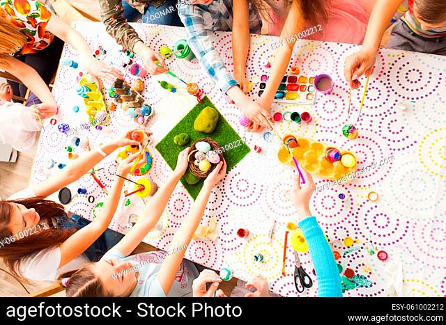 Top view of kids hands holding Easter crafts and colored eggs. Group of children working together creating Easter decorations
