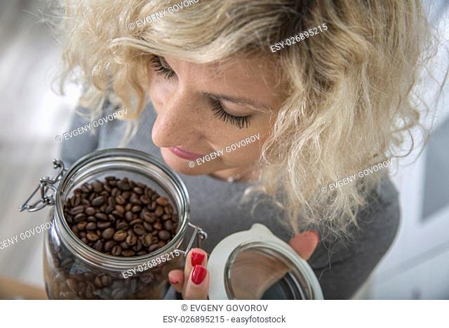 Blonde girl with curly hair is smelling coffee beans in glass pot