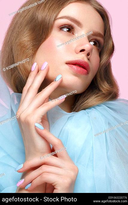 Beautiful girl with light make-up and gentle manicure in blue clothes. Beauty face. Design nails. Photo taken in studio on pink background