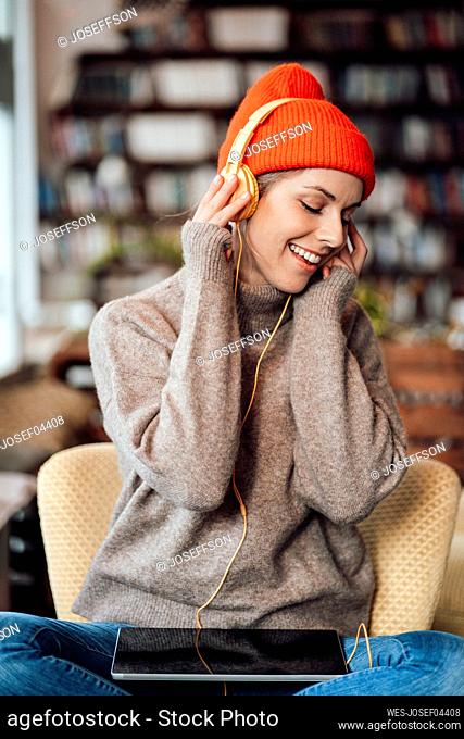 Happy businesswoman listening music through headphones at cafe