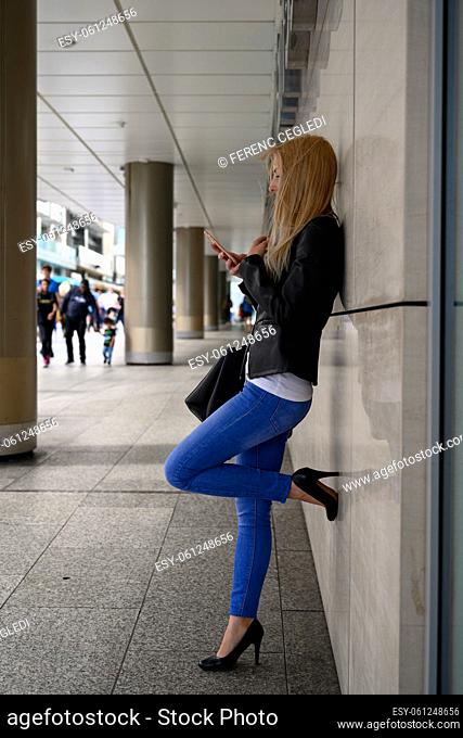 Attractive young urban checking her mobile phone while she is waiting outside of a business building in the business district of London, United Kingdom