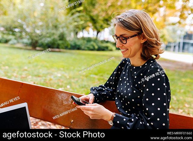 Smiling female freelancer text messaging through smart phone in public park