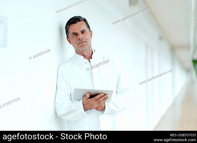 Scientist with tablet PC leaning on wall at medical clinic