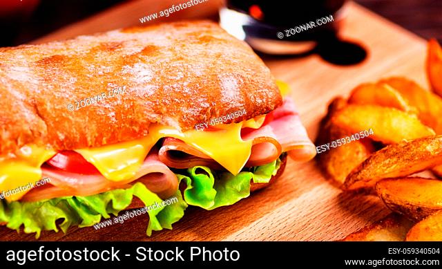 Sandwich with bacon, cheese, tomato, salad and potato wedges fried close-up on restaurant table