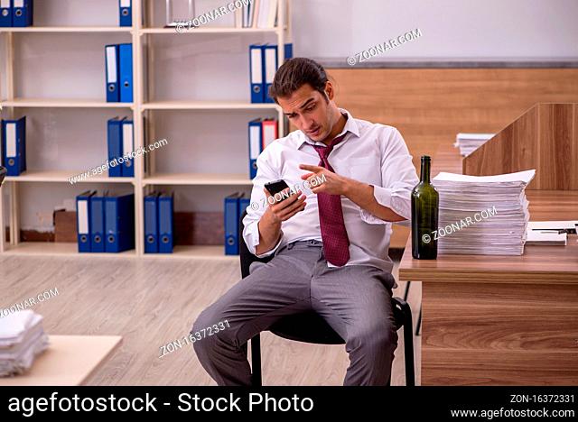 Young employee drinking alcohol in the office