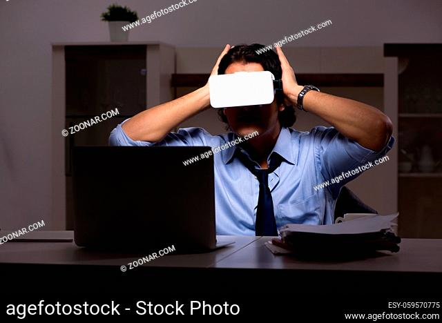 Young employee with virtual glasses at night in the office