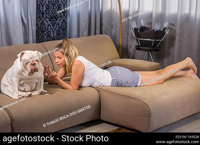 Young woman using smartphone on sofa with pet dog (english bulldog)