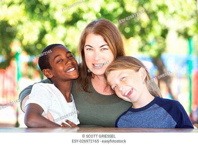Joyful single parent sitting in between adopted child and son at table in park