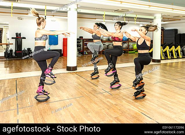 Group of female athletes in activewear and jumping shoes stretching out arms and hopping on spot during fitness training with instructor in gym