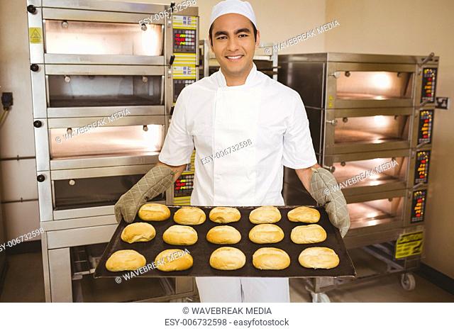 Baker smiling at camera holding tray of rolls