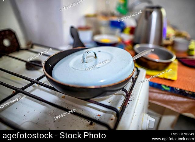 Kitchen interior in an old country house. An old small frying pan covered with a lid stands on a dirty gas stove
