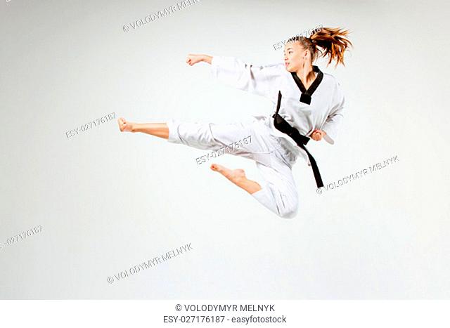 The karate girl in white kimono and black belt training karate over gray background
