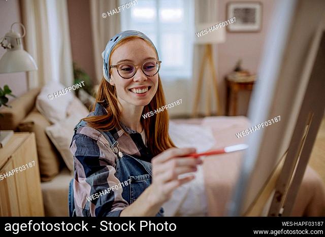 Happy woman wearing eyeglasses and bandana practicing painting at home