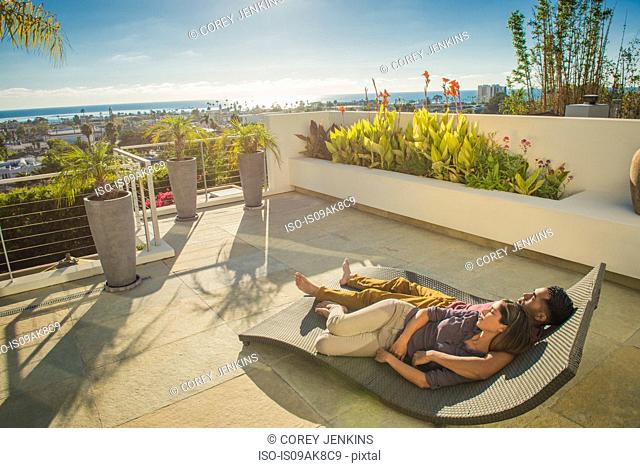 Couple lying on sun lounger in penthouse rooftop garden, La Jolla, California, USA