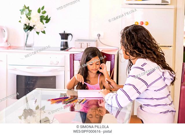 Teenage girl drawing with her little sister at table