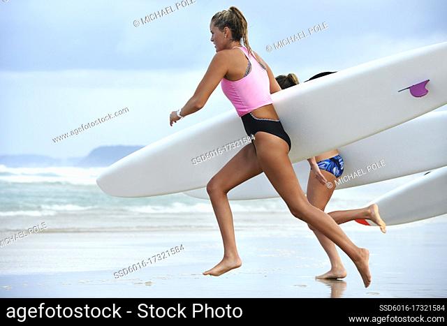 Side view of team of female surf lifeguards training and running into sea holding ocean surf skis