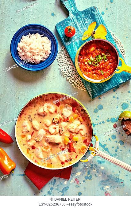Top down view of tasty Brazilian cuisine of shellfish, rice, tomato and other ingredients in pot and bowls on colorful table