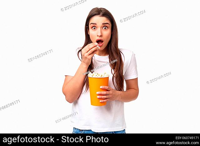 Entertainment, fun and holidays concept. Portrait of astonished and excited impressed young girl watching awesome movie, look astonished eating popcorn